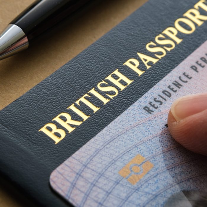Finger pointing at Biometric Residence permit Card (ILR, Indefinite leave to Remain) placed on top of British passport. Concept for naturalization. Stafford, United Kingdom, July 20, 2022